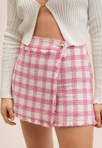 Roze-witte geruite minirok van gestructureerde stof, met franjes aan de randen en een gouden knoopsluiting aan de zijkant.