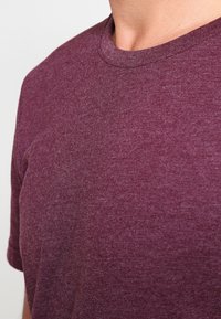 Kurzärmeliges T-Shirt mit Rundhalsausschnitt in tiefem Bordeauxrot, aus weichem, strukturiertem Stoff mit meliertem Muster.