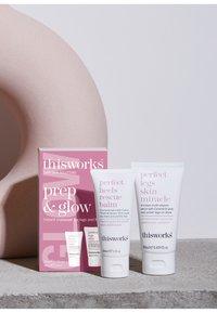 Sæt af tre hudplejeprodukter fra This Works i en pink og hvid emballage. Indeholder tuber til en balm og et tonet serum på en tekstureret grå overflade.