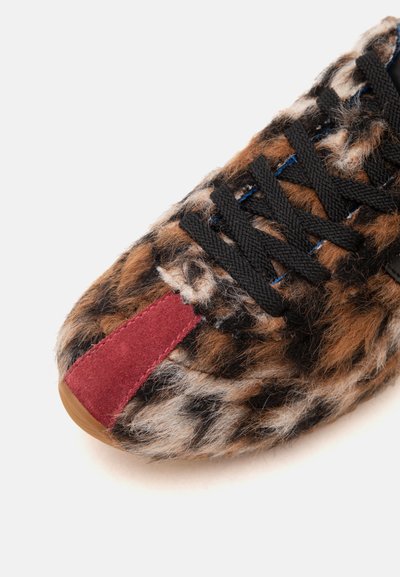 Gros plan d'une chaussure en tissu imprimé léopard marron et noir, lacets noirs et détail de bout en daim rouge.