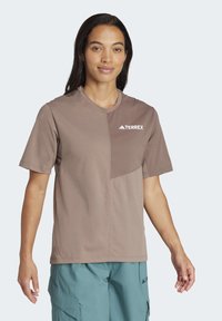 Brun kortærmet t-shirt med rund hals, der har et tekstureret patch og hvid Terrex-logo på brystet. Glat stof, afslappet pasform.