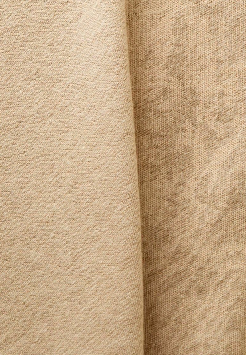 Beiger Strickstoff mit weicher Textur und sichtbaren feinen Fasern, sanft in weichen Falten drapiert.