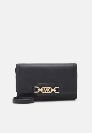 Portefeuille en cuir noir avec détail chaîne dorée et logo MK sur le devant, avec une lanière pour poignet sur un fond clair uni.