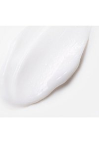 Dikke, glanzende witte crème textuur uitgesmeerd over een glad oppervlak, met een lichte glans en een zachte consistentie, wat wijst op een hydraterend product.