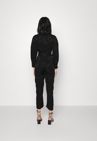 Svart jumpsuit med blommönster, långa ärmar, åtsittande midja och avsmalnande ben. Bärs med sandaletter med klack och remmar.