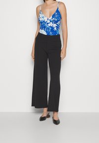 Blue floral bodysuit with thin straps, paired with high-waisted black wide-leg trousers and black slip-on shoes.