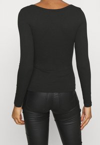 Czarna prążkowana bluzka z długim rękawem i szerokim dekoltem, dopasowany fason i gładka tekstura, w zestawie z eleganckimi czarnymi spodniami przypominającymi skórę.