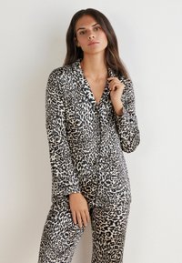 Pyžamo s leopardím vzorem vyrobené z měkké tkaniny, které obsahuje košili na knoflíky s límcem a dlouhými rukávy, doplněné o odpovídající kalhoty.