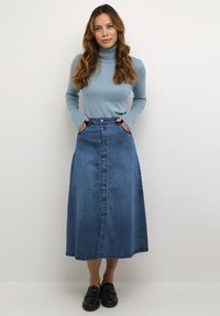 Gonna lunga in denim di taglio dritto, colore blu, chiusura anteriore con bottoni e tasche laterali. Accompagnata da un maglione a collo alto di un blu chiaro.