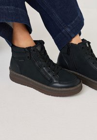 Zapatillas altas negras de cuero texturizado, con cremalleras laterales dobles y cordones, suela de goma marrón y diseño plano.