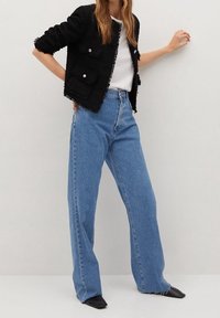 Musta tekstuuripintainen takki, jossa on kaksi etutaskua, valkoinen t-paita ja vaaleansiniset korkeavyötäröiset farkut. Mustat kärkitossut täydentävät asukokonaisuutta.