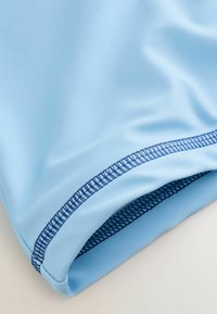 Pantaloncini atletici azzurri realizzati in tessuto liscio ed elastico con una rifinitura blu lungo l'orlo e dettagli in mesh all'interno.