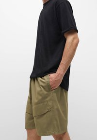 T-shirt noir en coton à manches courtes, associé à un short cargo vert olive clair avec plusieurs poches et une coupe décontractée.