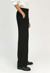 Pantalon noir ajusté à taille haute, avec poches latérales et coupe slim. Présente une texture lisse et un design à longueur complète.