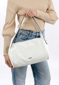 Weiße perforierte Handtasche mit schwarzen Akzenten, versehen mit seitlichen Reißverschlüssen und stabilen Tragegriffen. Der Stil hat eine weiche, strukturierte Form.