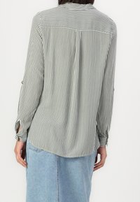Blusa a righe in verde chiaro e bianco, con polsini delle maniche abbottonati, orlo curvo e colletto con dettaglio in cucitura sul retro.