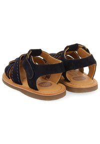 Navy blue suede sandals with open design, featuring stitching accents and a brown rubber sole. Adjustable straps for comfort and fit.