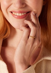 Gouden ring met een gestructureerd kraalontwerp, gedragen op een hand, met gladde huid en een neutraal gekleurd kledingstuk op de achtergrond.