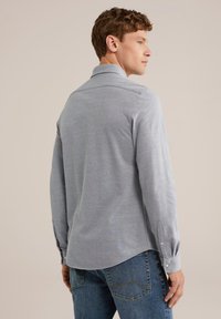 Világosszürke, hosszú ujjú ing gombos gallérral, sima textúrával és ívelt szegéllyel. Kék farmernadrággal párosítva.