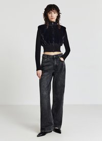 Schwarze Kunstpelz-verkürzte Jacke mit gerippten Ärmeln, kombiniert mit hochtaillierten, weit geschnittenen schwarzen Jeans und spitzen schwarzen Absätzen.