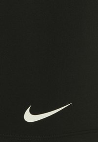 Musta venyvä kangas, jossa on voimakas valkoinen Nike-swoosh-logo vasemmassa alareunassa. Sileä ja napakka rakenne.