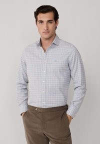 Button-up Hemd im blau-weißen Karomuster, mit spitzem Kragen und langen Ärmeln. Getragen mit einer braunen Cordhose.