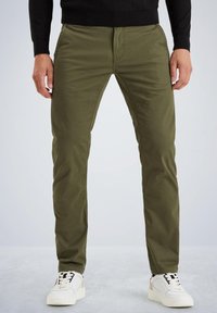 Chinos vert olive avec une coupe slim, fabriqués en coton doux, dotés de poches latérales et d'une fermeture éclair, accompagnés de baskets blanches.