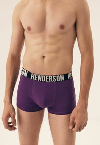 Fioletowe bokserki wykonane z miękkiego materiału z czarnym pasem z napisem "HENDERSON" w białej literze. Gładka tekstura i dopasowany krój.