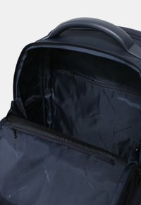 Interno dello zaino navy con superficie liscia, dotato di una tasca con zip e una fodera decorata con il marchio. Cerniera e maniglia robuste.