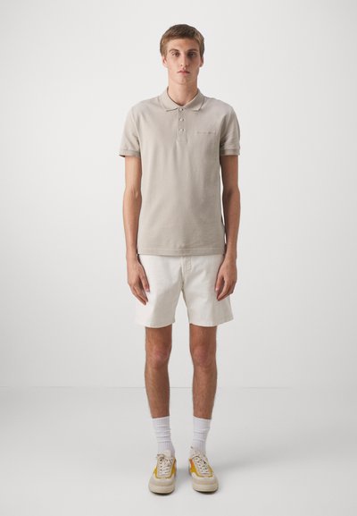 Helebeige polo-särk, millel on kolmest nööbist koosnev nööbirea, koos valgete lühikesed pükstega. Riietus sisaldab valgeid sokke ja beeže jalanõusid kollaste aktsentidega.