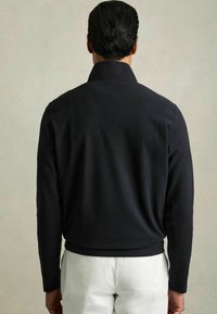 Suéter de un tono azul marino oscuro con textura de canalé, que presenta un cuello alto y mangas largas, ajustado en la cintura, mostrado desde la parte trasera sobre un fondo neutro.