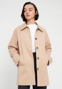 Μπεζ παλτό με κουμπιά, κατασκευασμένο από λείο ύφασμα, διαθέτει κλασικό γιακά, πλαϊνές τσέπες και άνετη εφαρμογή, με επένδυση στο εσωτερικό.