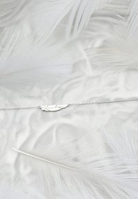 Söljefjäderarmband på vita fjädrar, med en delikat kedja och intrikat utformad fjäderberlock med slät textur.