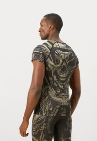 Fitted athletic shirt in black and olive green, featuring a bold skull graphic. Made from a smooth, stretchy fabric with a crew neckline.
