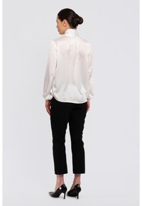 Seidenbluse in Elfenbein mit hohem Kragen und gerafften Ärmeln. Kombiniert mit schwarzen, schmalen Hosen und schwarzen High Heels.