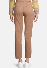 Ljusbruna rakbeniga byxor med bakfickor, slät textur och medelhög passform. Matchas med vita sneakers, sedd från baksidan.