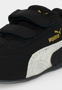 Μαύρο αθλητικό παπούτσι Puma με λευκή πλαϊνή λωρίδα, δύο μαύρα λουράκια με βέλκρο και χρυσό λογότυπο Puma στο πλάι και στη γλώσσα.