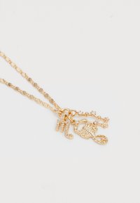 Guldtonet halskæde med et kædedesign, der har dekorative charms: en skorpion, et bogstav "M" og en funklerende nøgle.