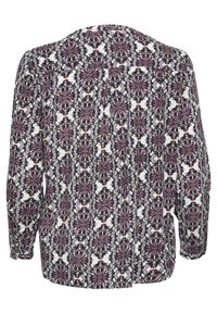 Blouse à manches longues avec un motif floral symétrique répétitif en violet, noir et marron sur fond blanc.