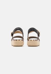 Sandalias de esparto de cuero negro con suela de yute trenzado, correa trasera para el tobillo y detalle de hebilla en tono dorado. Superficie suave y diseño abierto.