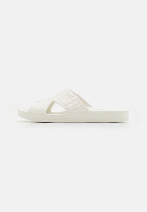 White slide sandal with textured upper, crossed straps, and a ridged sole. Made from lightweight material, featuring open sides for ventilation.