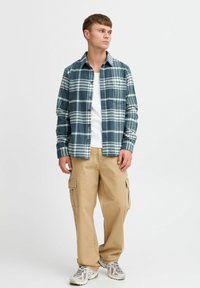 Blue and white plaid flannel shirt with a chest pocket, paired with khaki cargo pants featuring side pockets, and gray sneakers.