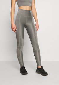 Legginsy sportowe z wysokim stanem w teksturowanym szarym materiale z kontrastowymi detalami, zestawione z pasującym topem cropped i czarnymi sneakersami.