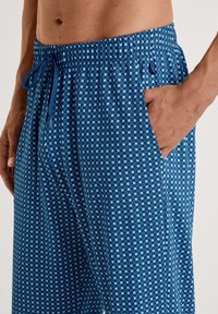 Blauwe loungebroek met patroon en een koord in de taille, met kleine vierkanten in lichtere blauwtinten en zijzakken. Gemaakt van een lichtgewicht stof.