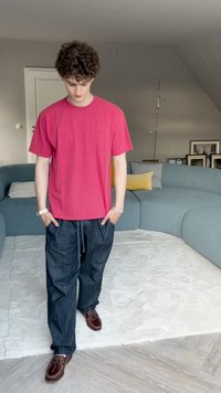 Vaaleanpunainen lyhythihainen t-paita, rento malli, yhdistettynä tummiin farkkuihin. Ruskeat kengät nauhoilla ja koristeellinen rannekoru ranteessa.