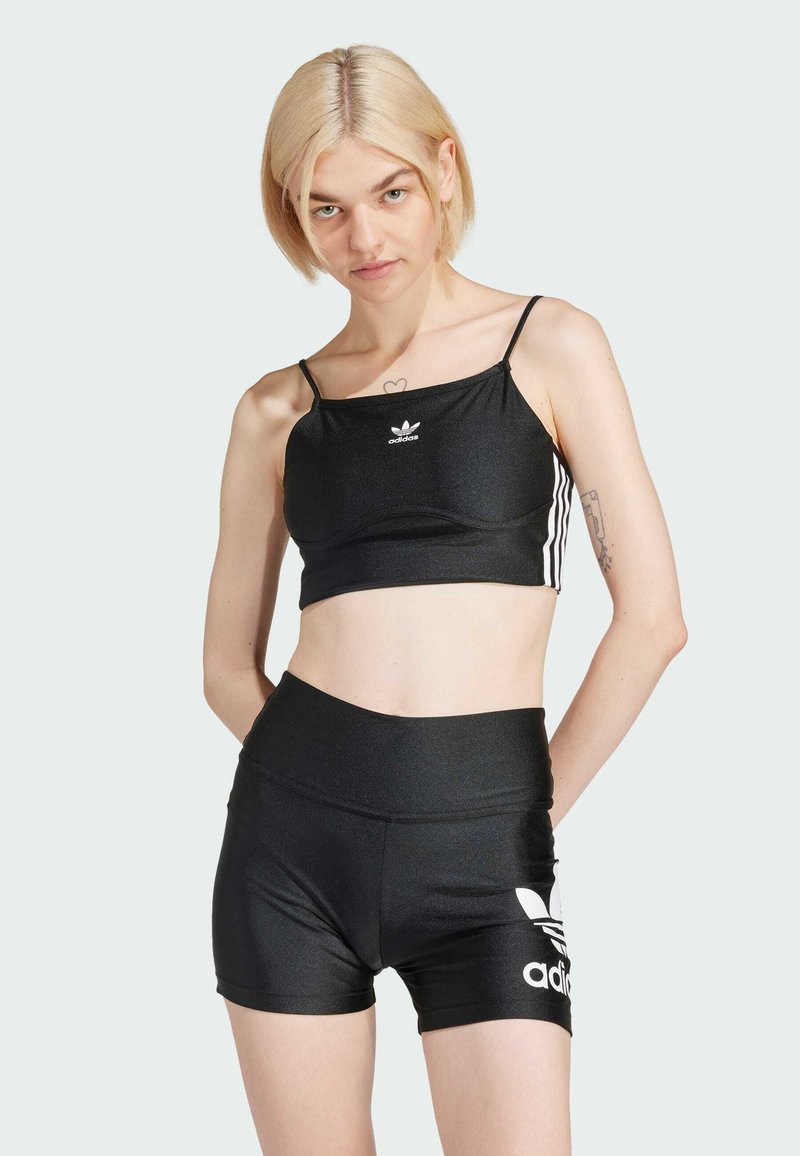 Top desportivo preto, cortado, com alças finas e logótipo branco, combinado com calções pretos de cintura alta com um emblema branco da marca. Textura suave.