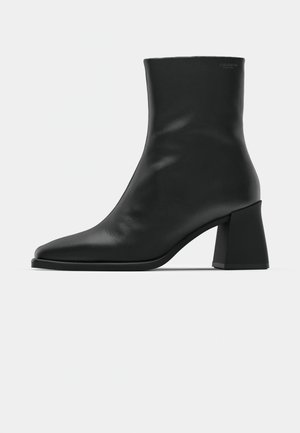 Black leather ankle boot with a pointed toe and a block heel. Smooth texture, minimalist design, and a high-cut silhouette.