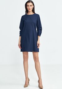 Granatowa sukienka w pionowe białe paski, okrągły dekolt, długie bufiaste rękawy oraz dopasowana góra, sięgająca powyżej kolan.