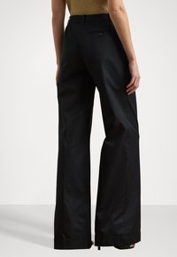 Black wide-leg trousers with a smooth texture, featuring a back pocket and folded hems. High-waisted design accentuates a tailored fit.