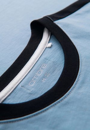 Lichtblauw T-shirt met een zwarte geribbelde kraag en witte details, met een label waarop het merk en de maat aan de binnenkant zijn gestikt.